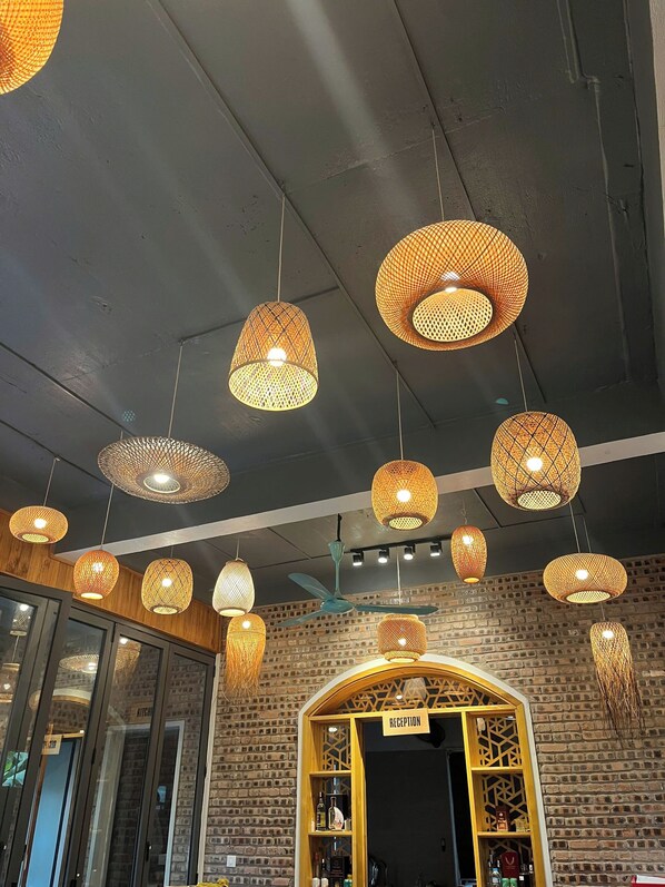 A restaurant interior with multiple hanging wicker lamps, a reception area, and a brick wall. - Duong Lam Village (Hanoi)