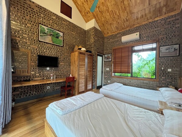 A room with two beds, a wooden desk, a TV, and a window with a view of greenery. - Duong Lam Village (Hanoi)