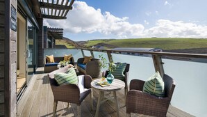 Una terraza con mobiliario de mimbre, una mesa y vistas a un lago y colinas.