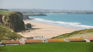 Vista costera con una playa arenosa, acantilados y un pueblo a lo lejos.