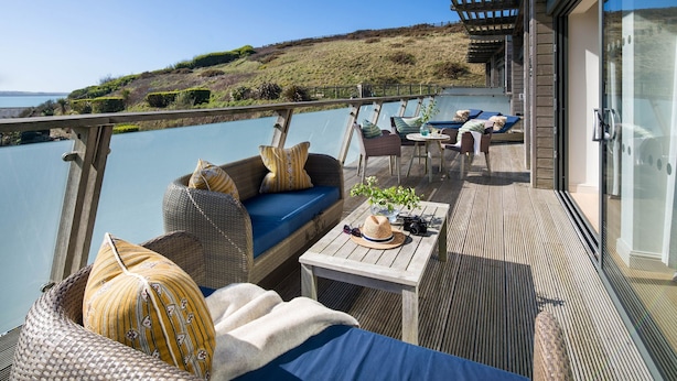 Una terraza con mobiliario de mimbre, una mesa con un sombrero y una cámara, y vista al mar.