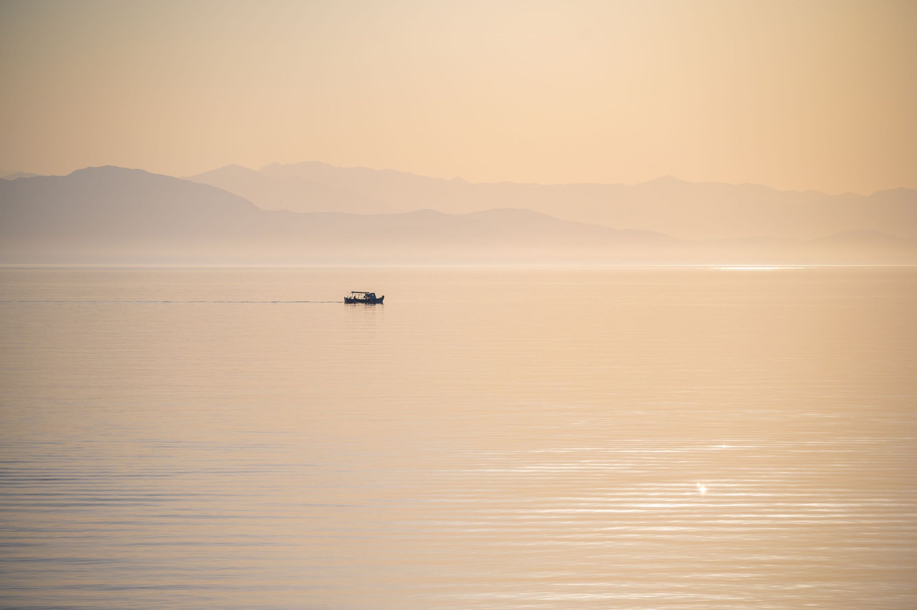 A calm body of water with a small boat in the distance and mountains in the background.