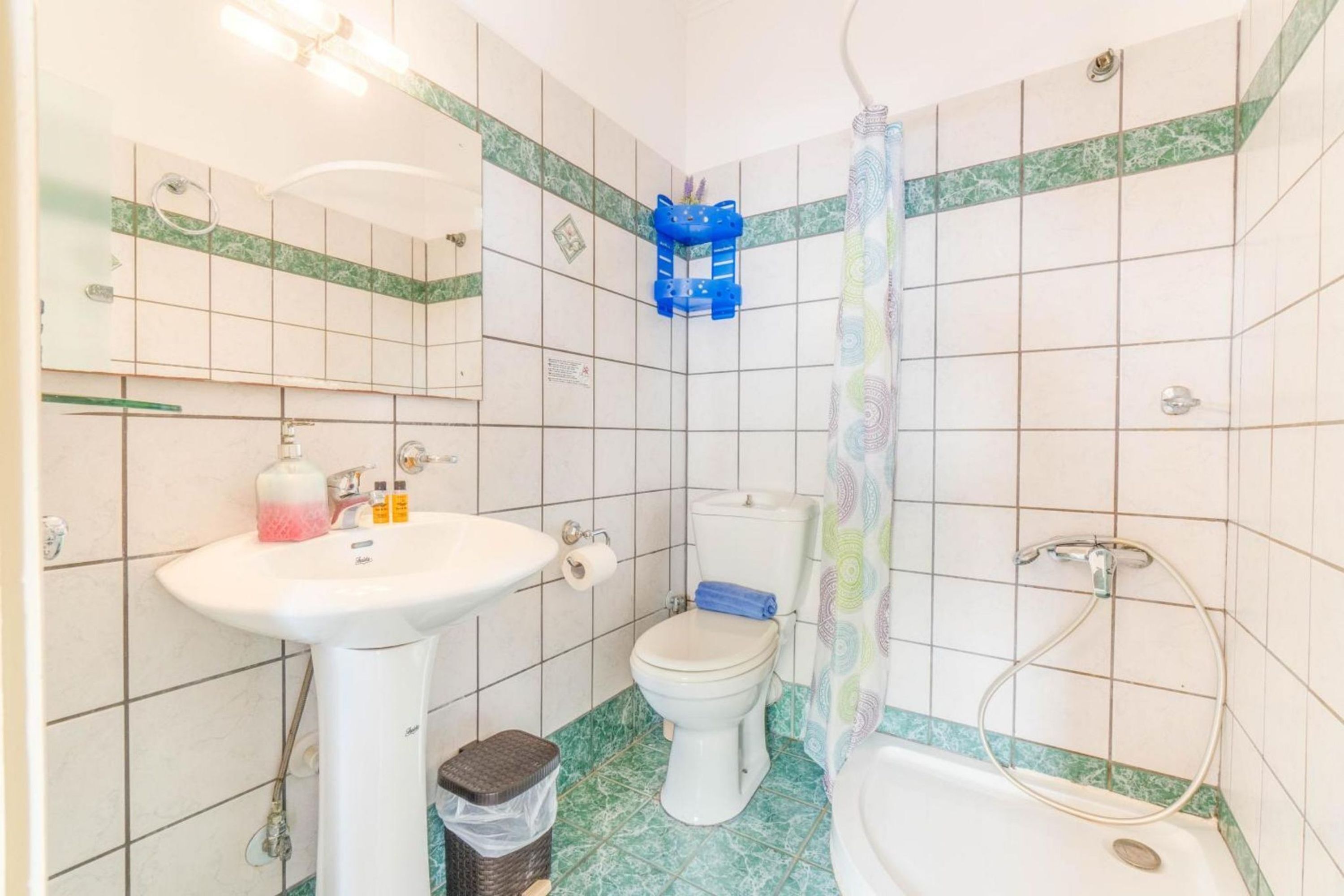 Une salle de bain avec un lavabo, des toilettes et une baignoire blancs, le tout agrémenté de carreaux blancs et verts.