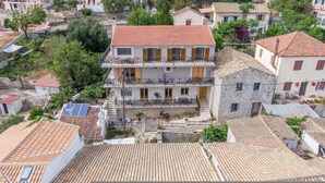A residential building with a red-tiled roof, a balcony with a black railing, and a stone facade. - Paxi Apt in Gaios With 1 Bedrooms and 1 Bathrooms (Paxos)