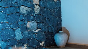 Una pared de piedra, un jarrón y una mesa de comedor con un vaso y un plato.