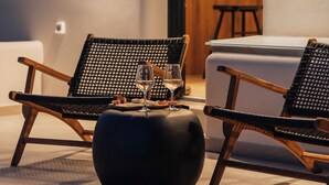 Un interior moderno con dos sillas de mimbre, un reposapiés negro y una copa de vino sobre una mesa.