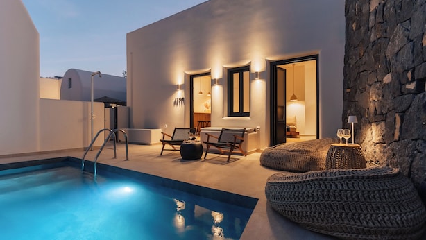 Un área de piscina moderna al aire libre con una pared de piedra, dos sillas de descanso y una pequeña mesa con vasos.