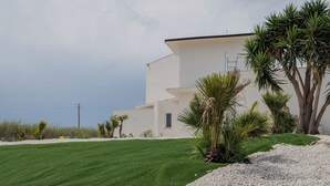 Un edificio moderno bianco con tetto piatto, circondato da un prato curato e palme.