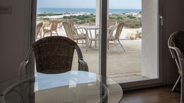 Un tavolo in vetro con sedie in vimini in una stanza con vista sulla spiaggia e sull'oceano.