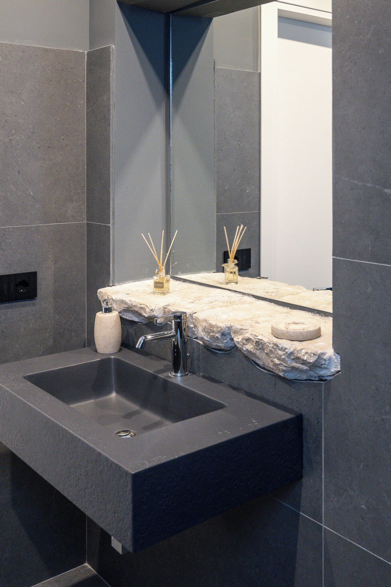 A modern bathroom with a dark sink, a mirror, and a stone countertop.