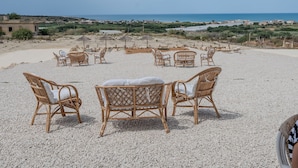 Zona relax in spiaggia con sedie in vimini e ombrelloni, affacciata su un paesaggio costiero.