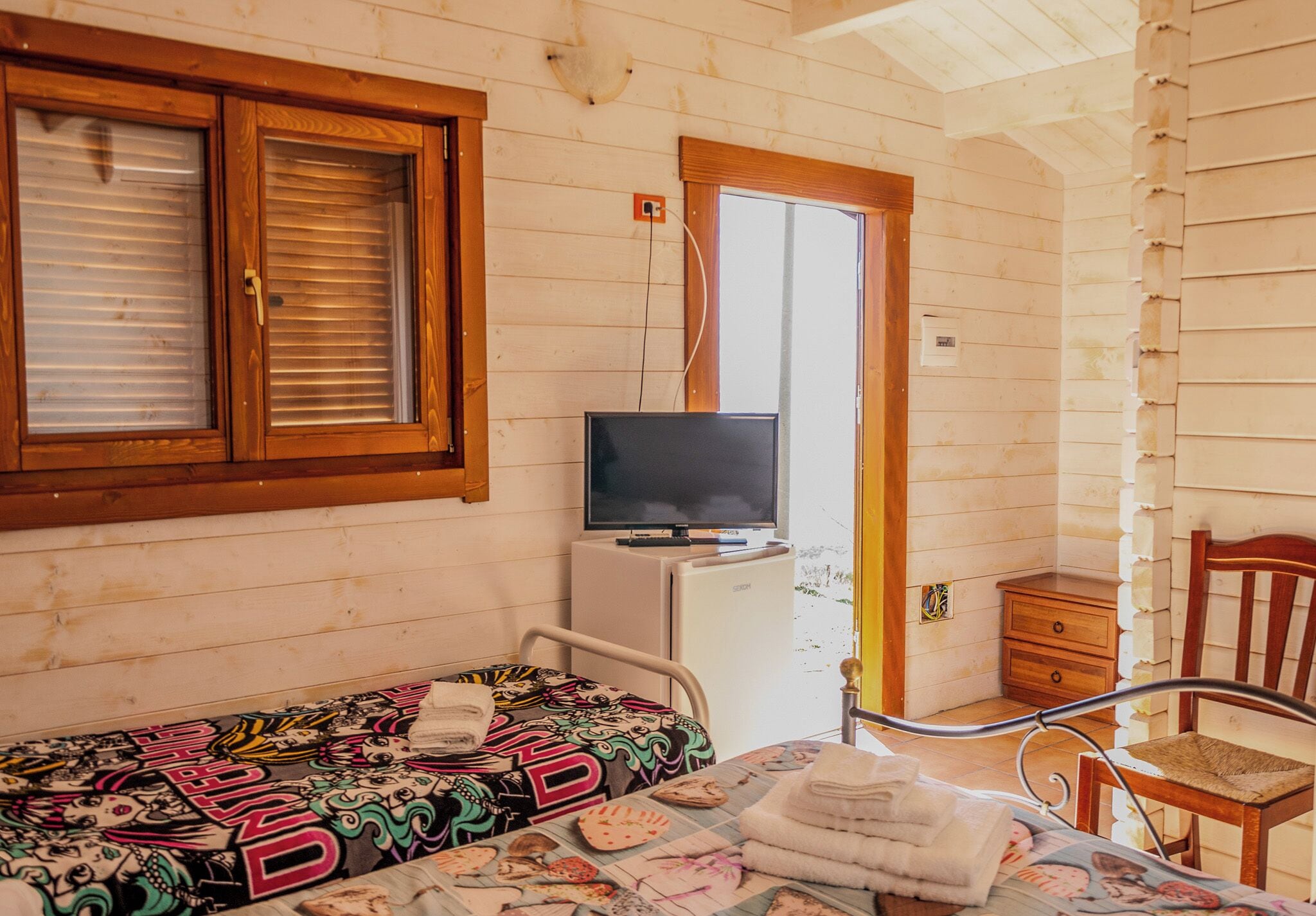 Ein Zimmer mit einem Bett, einem Fernseher auf einer Kommode, einem Sessel und einer Tür, die nach draußen führt.