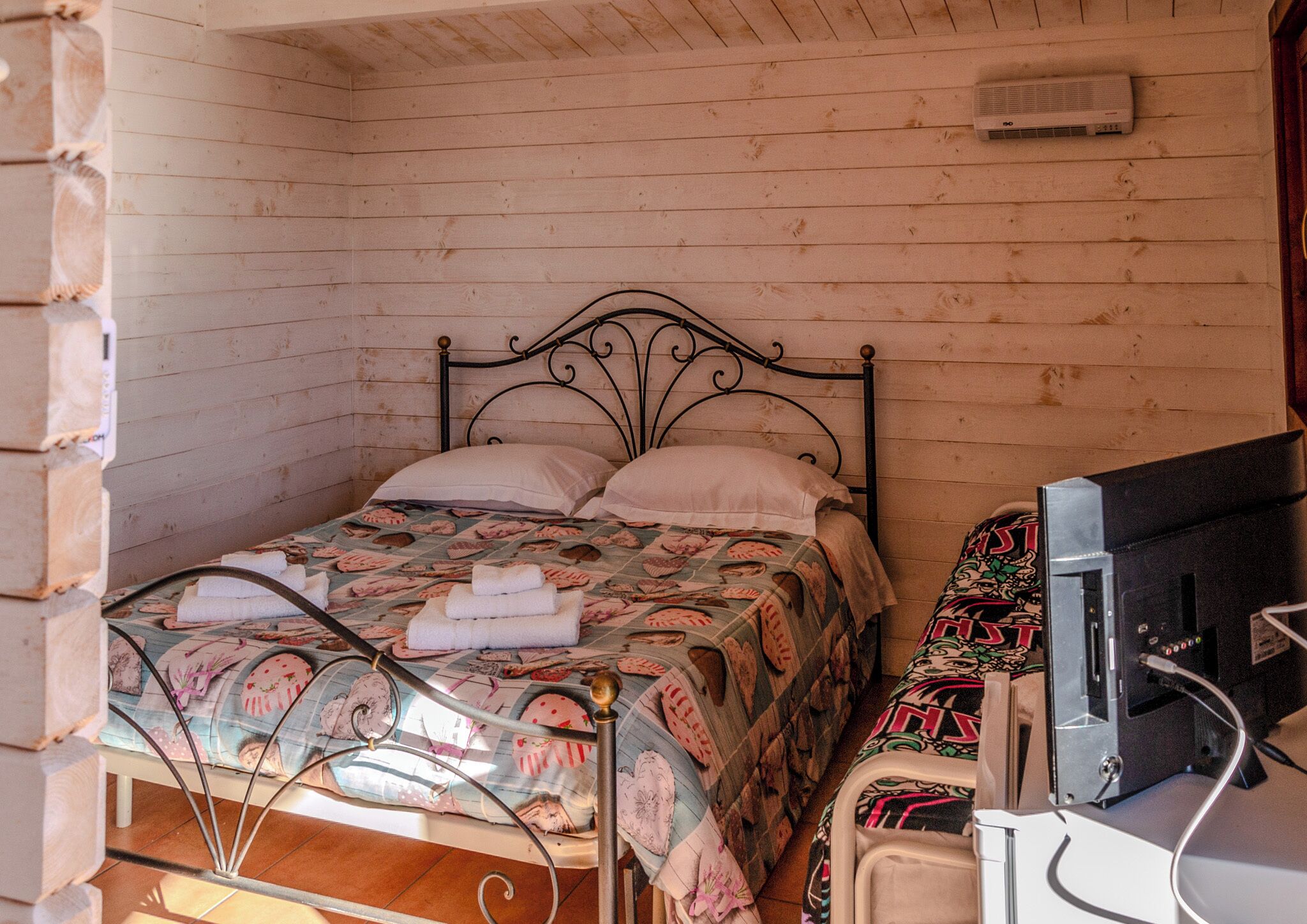 A wooden cabin room with a bed, a television, and a small table.