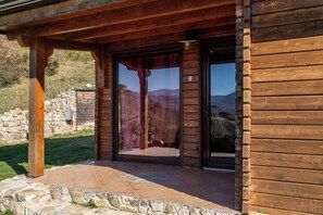 Una cabaña de madera con un muro de piedra y un ventanal que da a un patio.