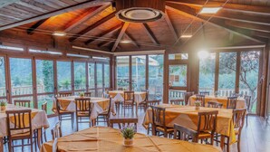 A restaurant with multiple tables and chairs, large windows, and a wooden ceiling.