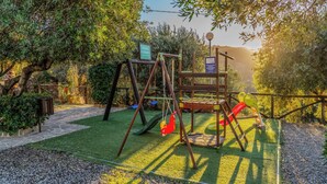 A playground with swings and slides, surrounded by trees and a stone pathway.