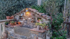 A stone-built outdoor kitchen with terracotta pots and a small sign.