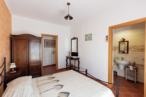 A bedroom with a bed, a wooden wardrobe, a desk with a laptop, a mirror, and a bathroom with a sink and toilet. - Agriturismo Radici Irpine (Rocca San Felice)