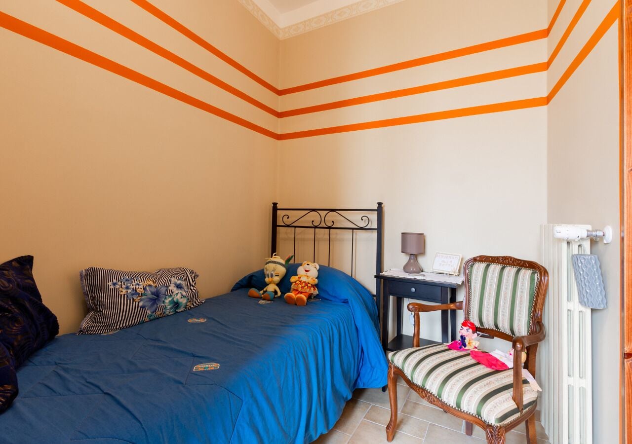 Een slaapkamer met een bed, een stoel, een nachtkastje en een dressoir.