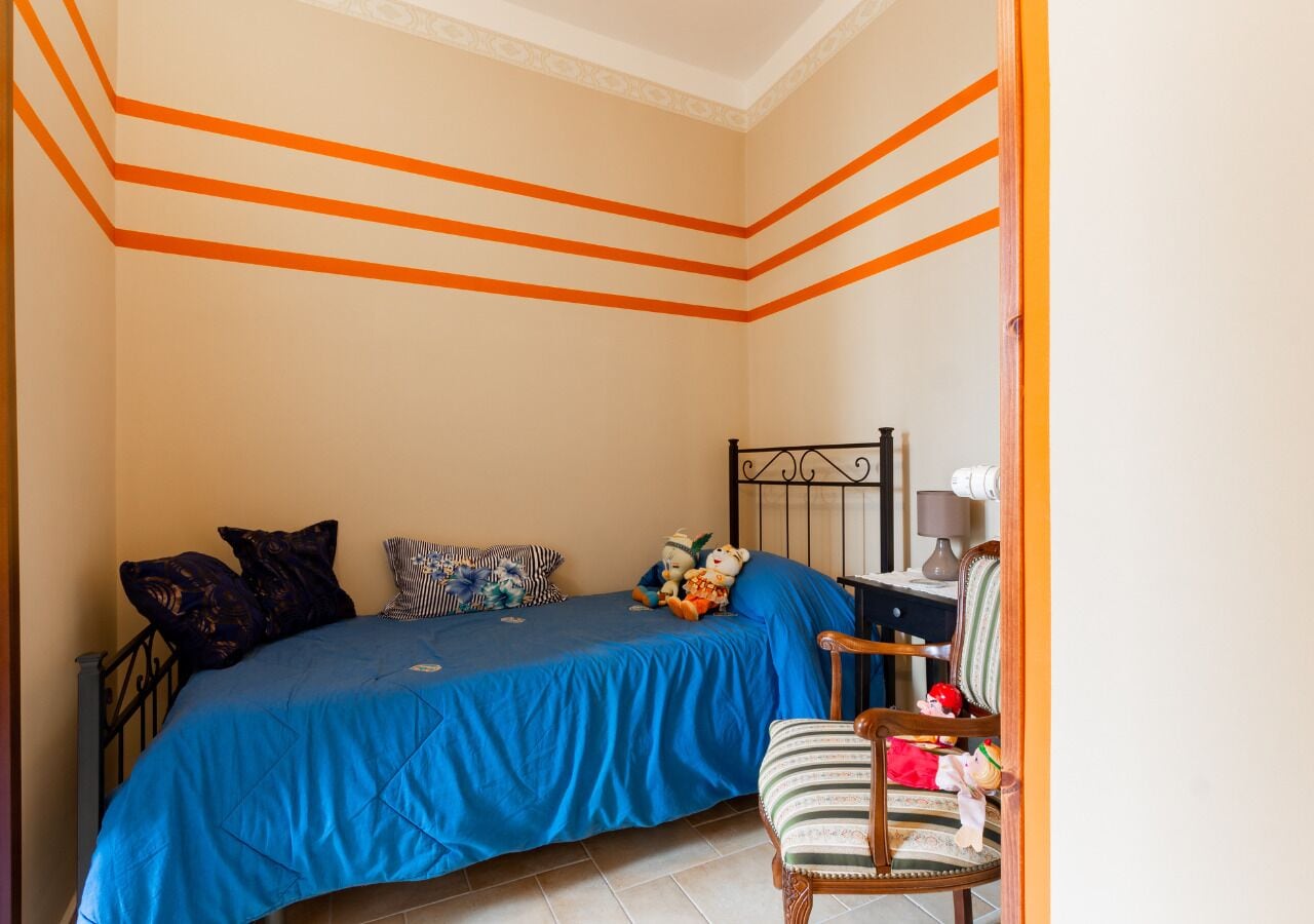 Une chambre à coucher avec un lit, des oreillers, des peluches, une chaise et un bureau avec une lampe.