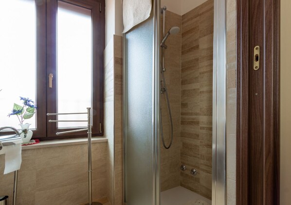 A modern bathroom with a glass-enclosed shower, a wooden vanity, and a window with a towel hanging on the door. - B&B la Botte (Taurasi)