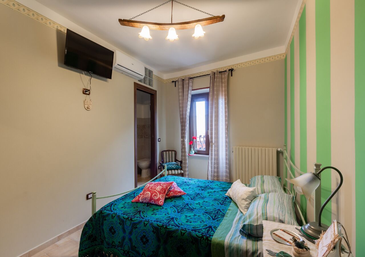 Un dormitorio con cama, escritorio, silla, televisor y ventana con cortinas.