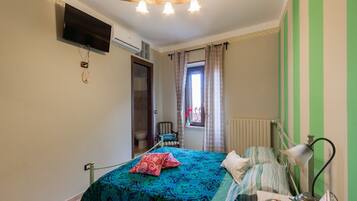 Un dormitorio con cama, escritorio, silla, televisor y ventana con cortinas.