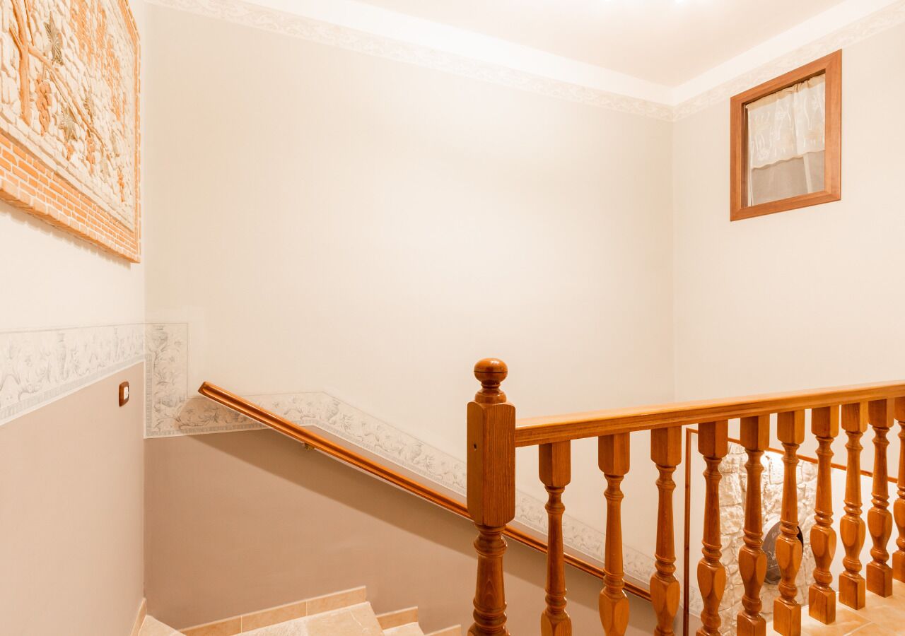 Un escalier avec des balustres en bois et une main courante, menant à un palier où est accroché un cadre photo au mur.