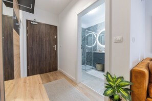 A modern bathroom with a glass shower, a wooden door, and a potted plant. - Sunny Bulevard Suite (Zadar)