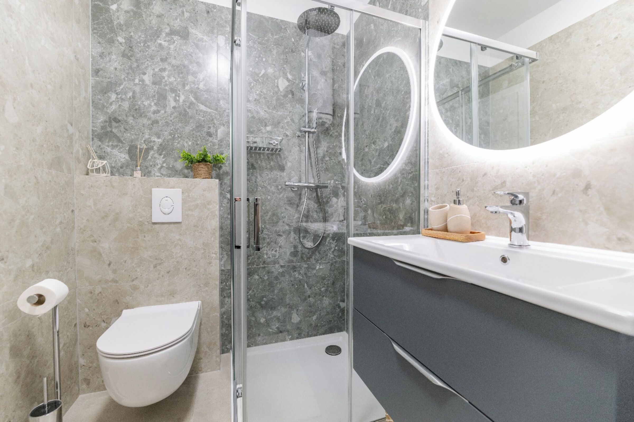 Ein modernes Badezimmer mit einer in Glas abgeschirmten Dusche, einer weißen Toilette, einem Waschtisch mit Spiegel und einer Marmorwand.