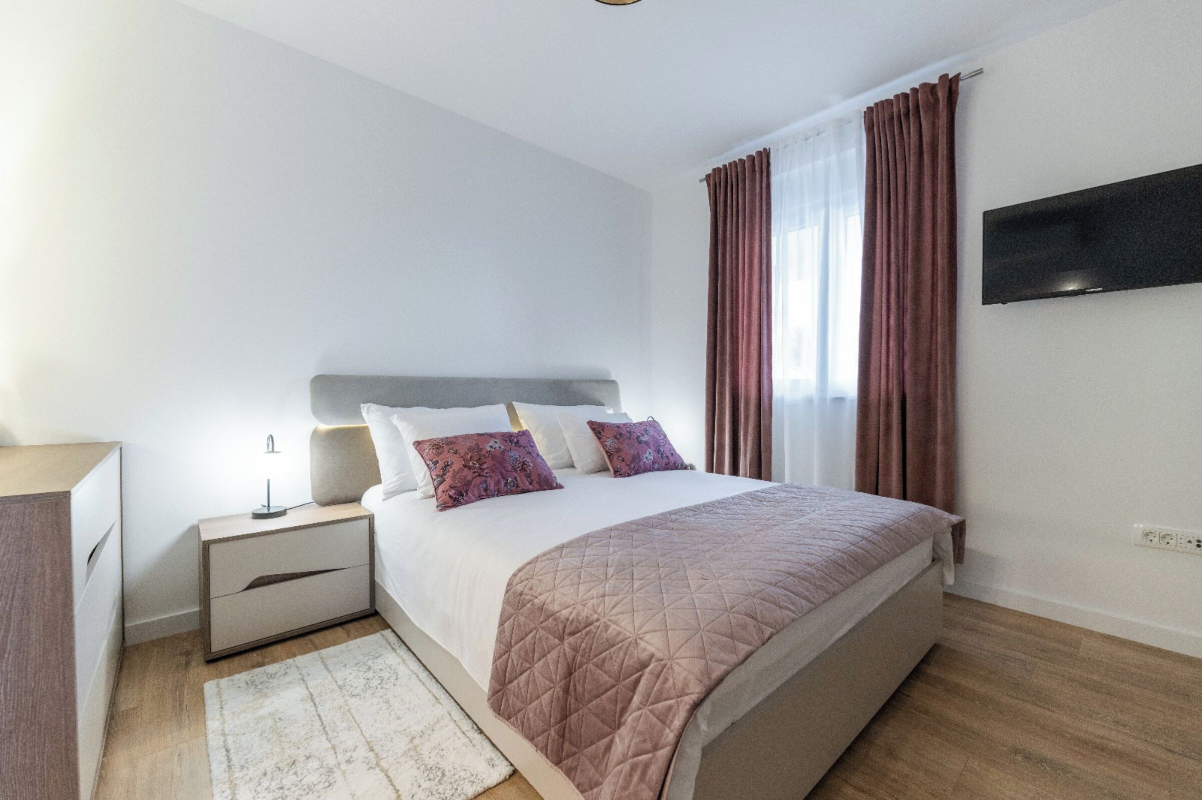 A modern bedroom with a bed, nightstand, and a TV mounted on the wall.