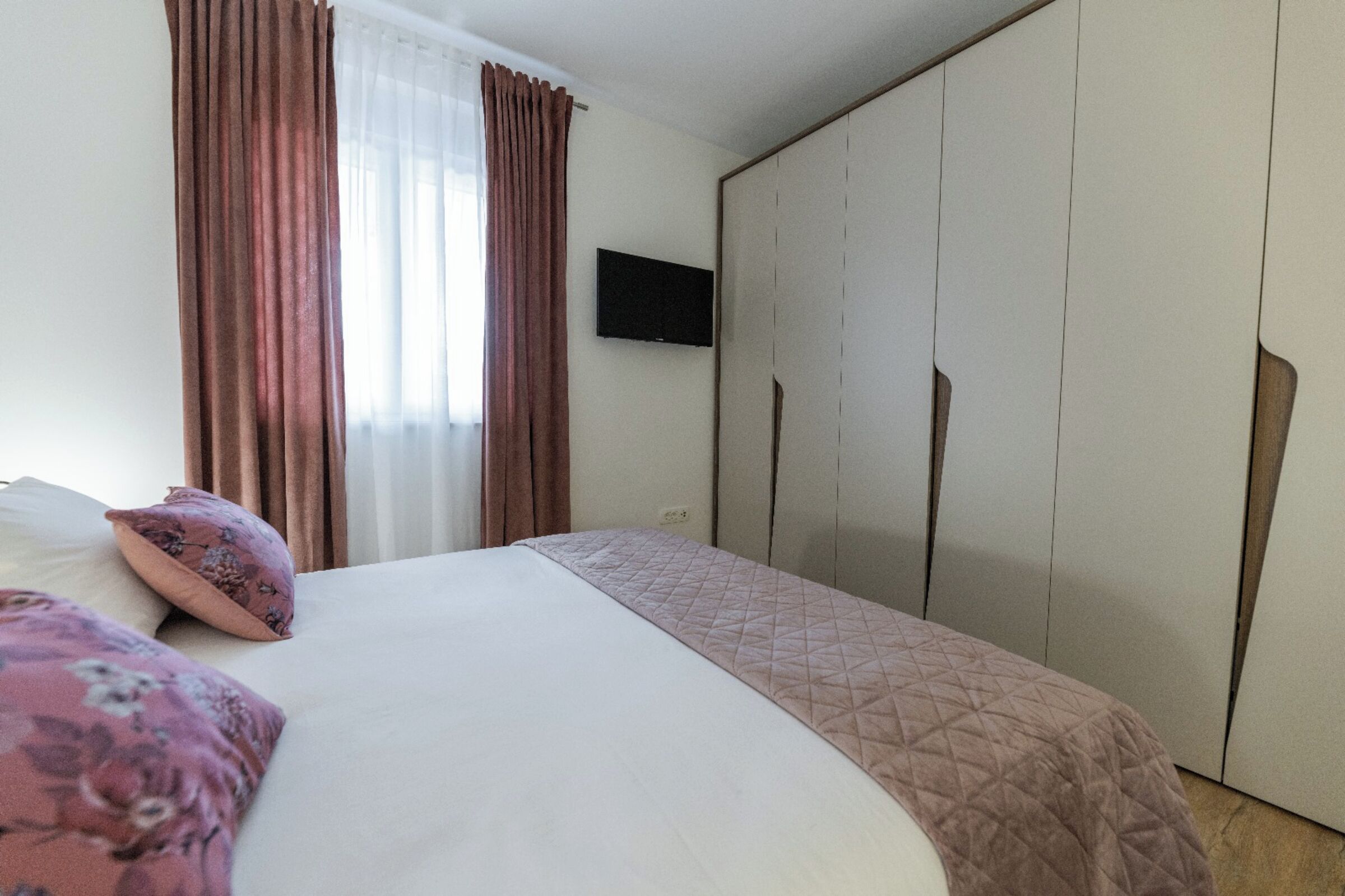 A bedroom with a bed, a TV mounted on the wall, and a wardrobe.