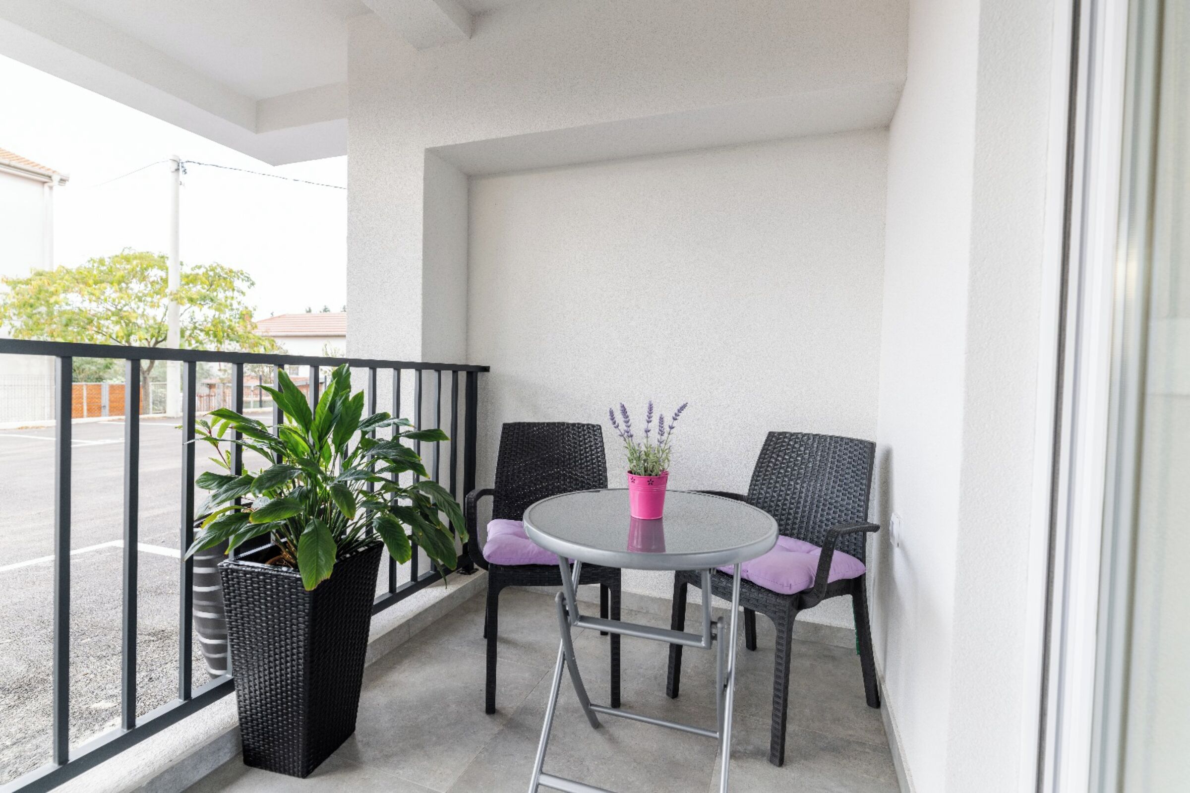 A balcony with two wicker chairs, a small round table, and a potted plant.