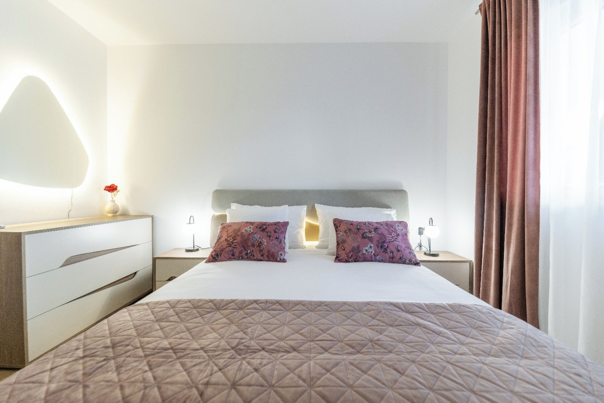 A hotel room with a large bed, two nightstands, a dresser, and a mirror.