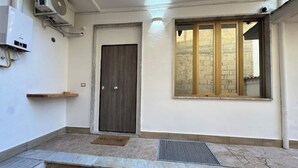 Ein sauberer, moderner Eingangsbereich mit einer dunklen Holztür, einem kleinen Fenster mit Blick auf die Straße und einer Fußmatte.