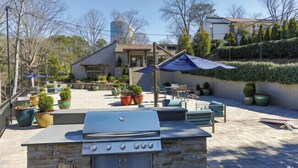 Une terrasse extérieure avec un barbecue en pierre, des plantes en pot et du mobilier d’extérieur.
