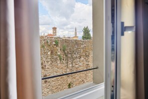 A view through a window of a stone wall with a clock tower and a spire in the background. - Casa Negroni, ancient house in front of medieval walls (Firenze)