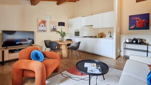 A modern living room with a TV, orange sofa, dining table, and kitchen area. - Casa Negroni, ancient house in front of medieval walls (Firenze)
