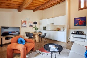 Una sala moderna con televisor, sofá naranja, mesa de comedor y zona de cocina.