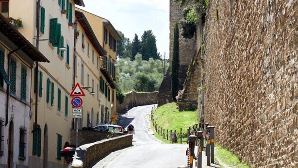 A narrow street with buildings on either side, a stone wall on the right, and a pedestrian crossing sign. - Casa Negroni, ancient house in front of medieval walls (Firenze)