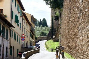A narrow street with buildings on either side, a stone wall on the right, and a pedestrian crossing sign. - Casa Negroni, ancient house in front of medieval walls (Firenze)