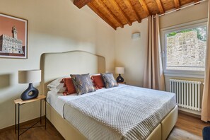A bedroom with a large bed, two bedside tables, a window with a view of a stone wall, and a wooden ceiling. - Casa Negroni, ancient house in front of medieval walls (Firenze)