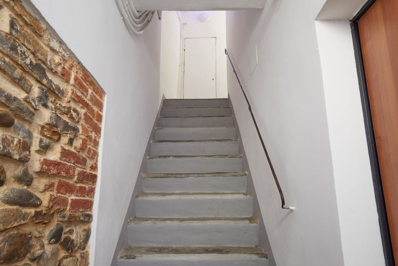 A staircase with a white door at the top, a stone wall on the left, and a wooden door on the right.