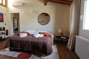 Un dormitorio con cama, un espejo redondo, una mesita de noche con lámpara y un radiador.