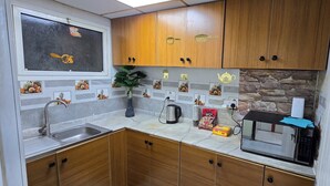 A compact kitchen with wooden cabinets, a stainless steel sink, a microwave, and a kettle. - Alharaki Capsule  (Dubai)