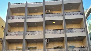 A multi-story building with balconies, a car parked in front, and a clear blue sky. - Alharaki Capsule  (Dubai)