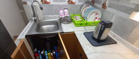 A modern kitchen with a built-in sink, a dish rack, and a drawer with water bottles.