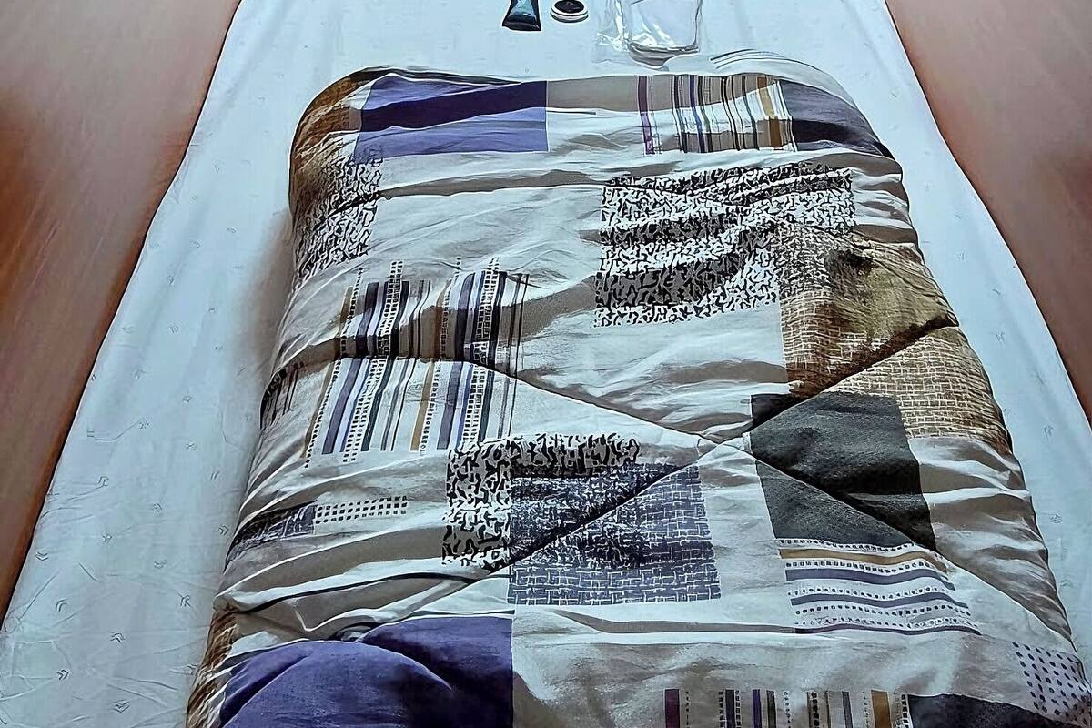 A single bed with a quilted blanket, a pillow, and a bedside table with a lamp.