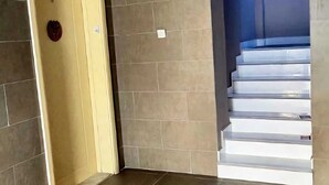 A room with a yellow door, tiled walls, and a staircase leading to a blue area. - Alharaki Capsule  (Dubai)