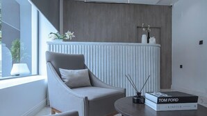 A modern living room with a grey armchair, a round coffee table with a book, and a radiator with decorative items. - Twenars Apartment  (Abuja)